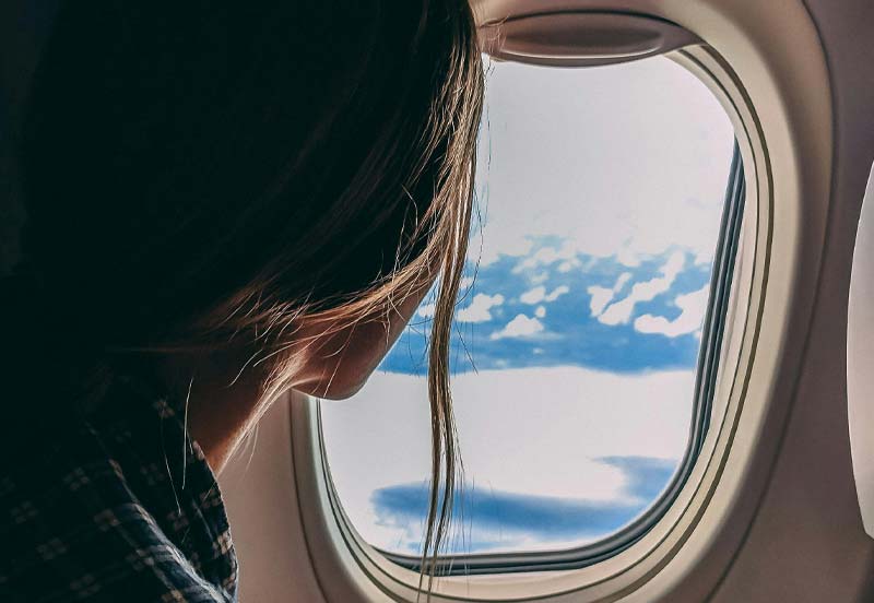 Mujer joven frente a la ventana de un avión en Aquitania