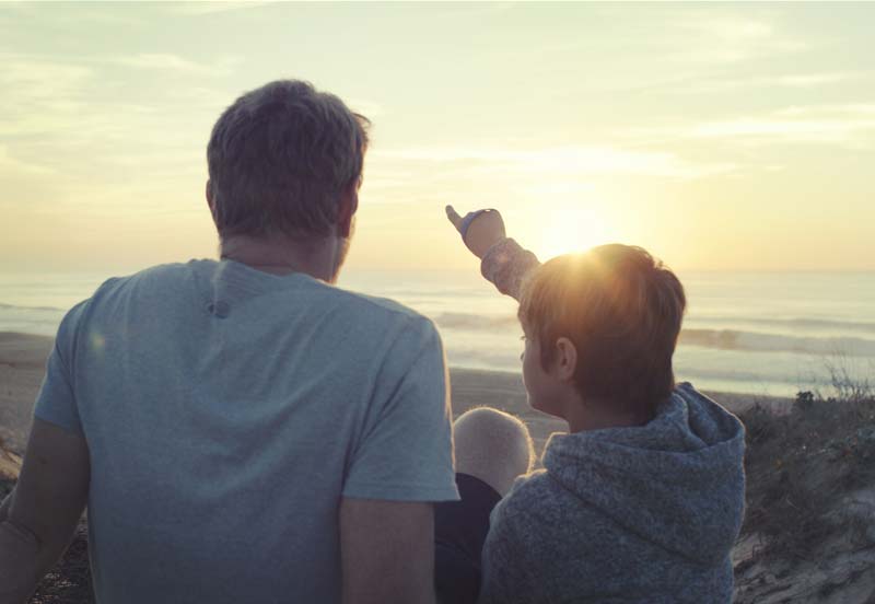 Padre e hijo contemplando una puesta de sol en una playa cerca del camping en las Landas